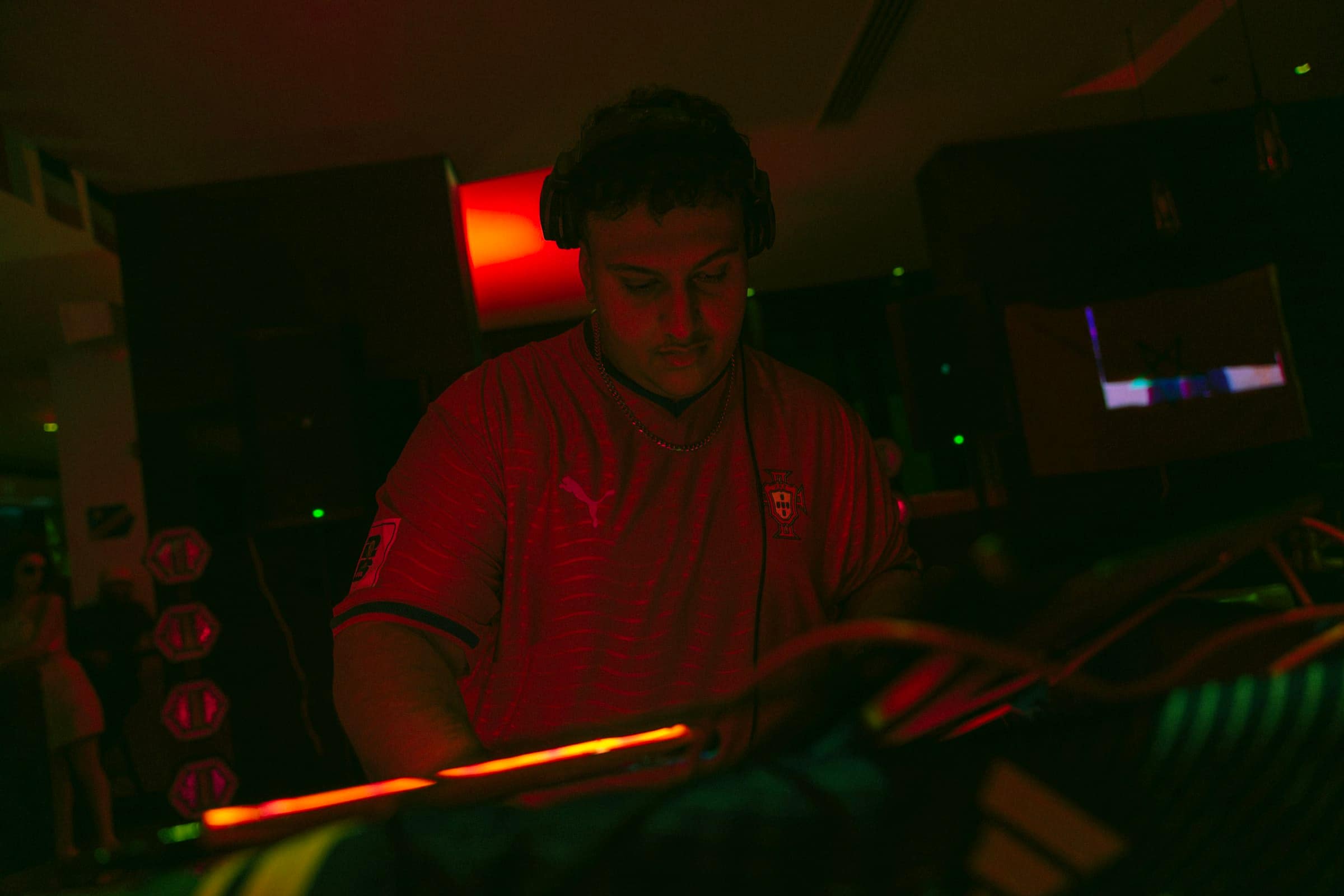 A DJ in headphones working the controls, the room dark and red behind.